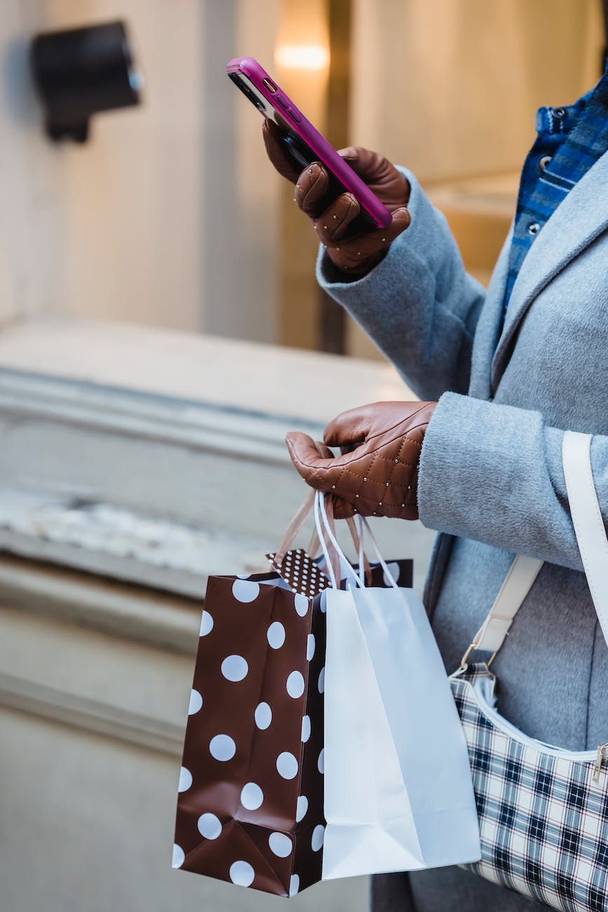 crop woman with shopping bags browsing smartphone on street